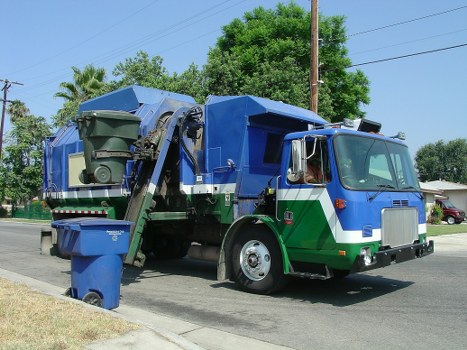 Large clearance truck handling bulky garden waste near a suburban property