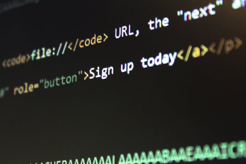 Close-up photograph of a computer screen showing lines of programming code with syntax highlighting in various colors, including orange, green, purple, pink, and yellow, set against a dark background.